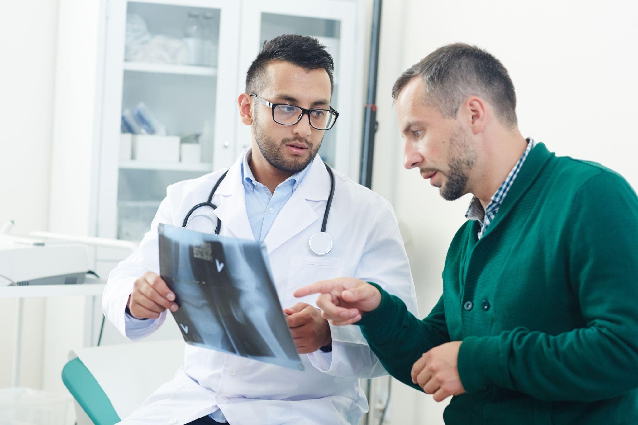 A male doctor is discussing with the male patient his x-ray of his joints in his clinic.
