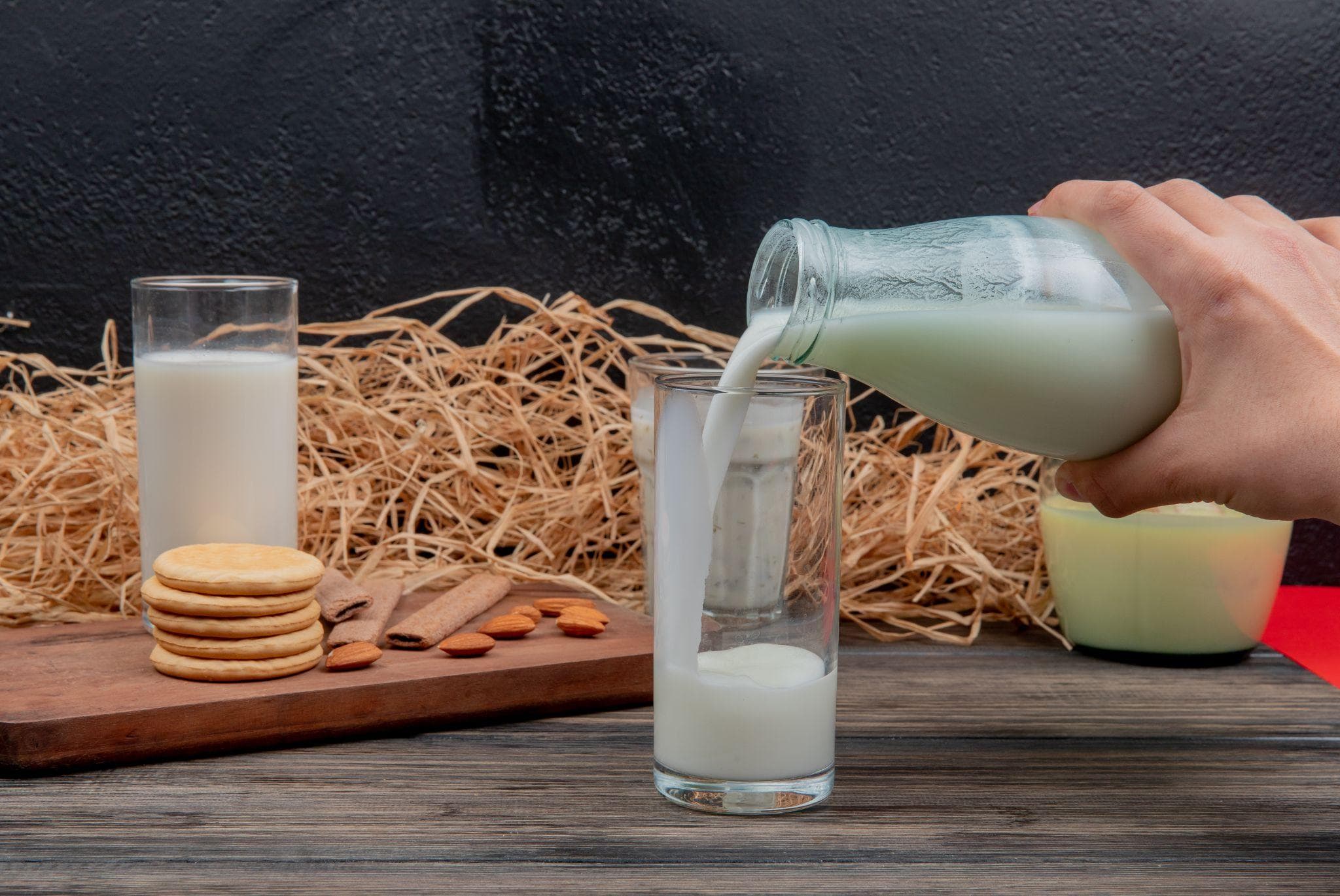 Hand pouring milk from a bottle into a glass with cookies and almonds on the table.
