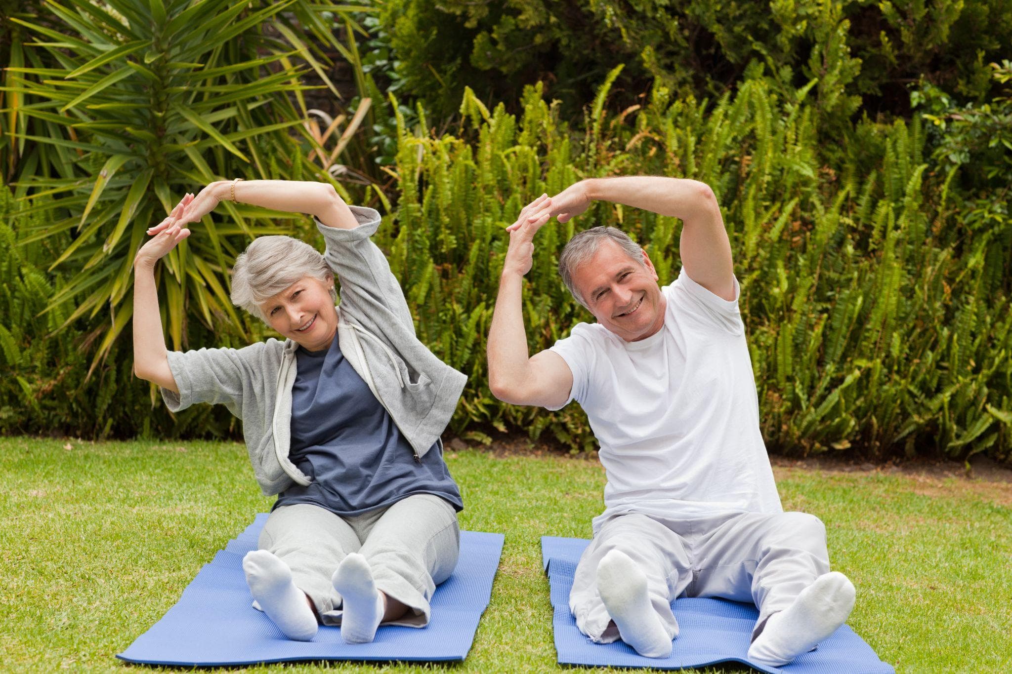 Senior couple doing stretching exercises on yoga mats in a garden.