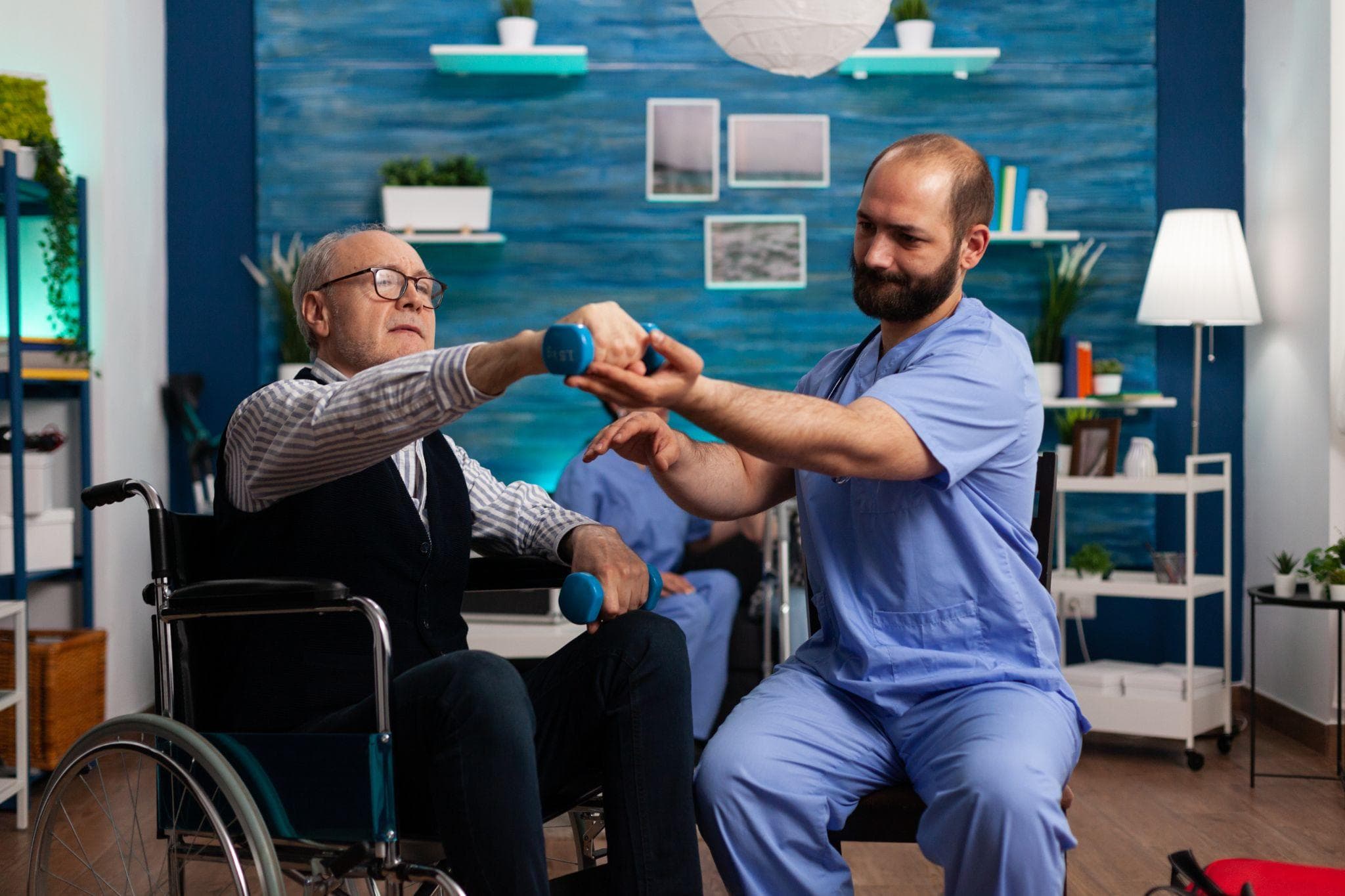 Physiotherapist assisting a senior man in a wheelchair with strength exercises using dumbbells.