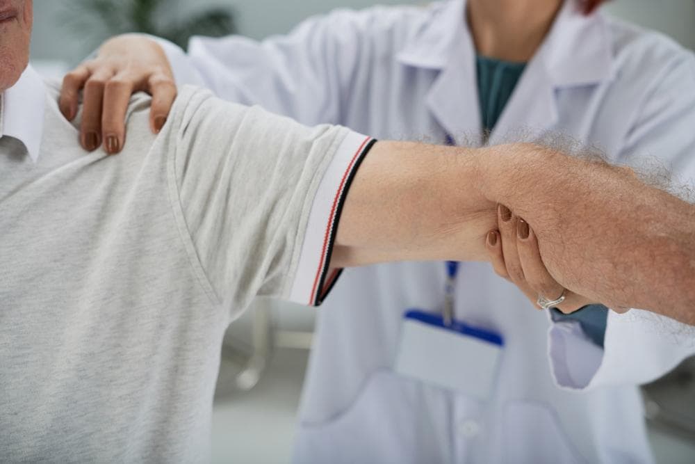 A female doctor is examining a male patient's shoulder in the clinic.