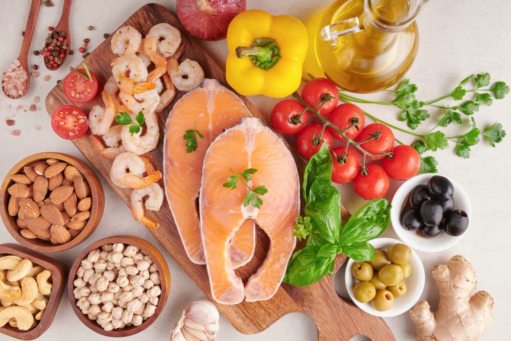 ** Healthy food assortment with salmon, shrimp, almonds, chickpeas, tomatoes, olives, basil, and olive oil.