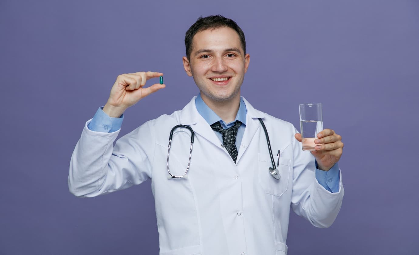 ** Smiling male doctor holding a capsule and a glass of water.