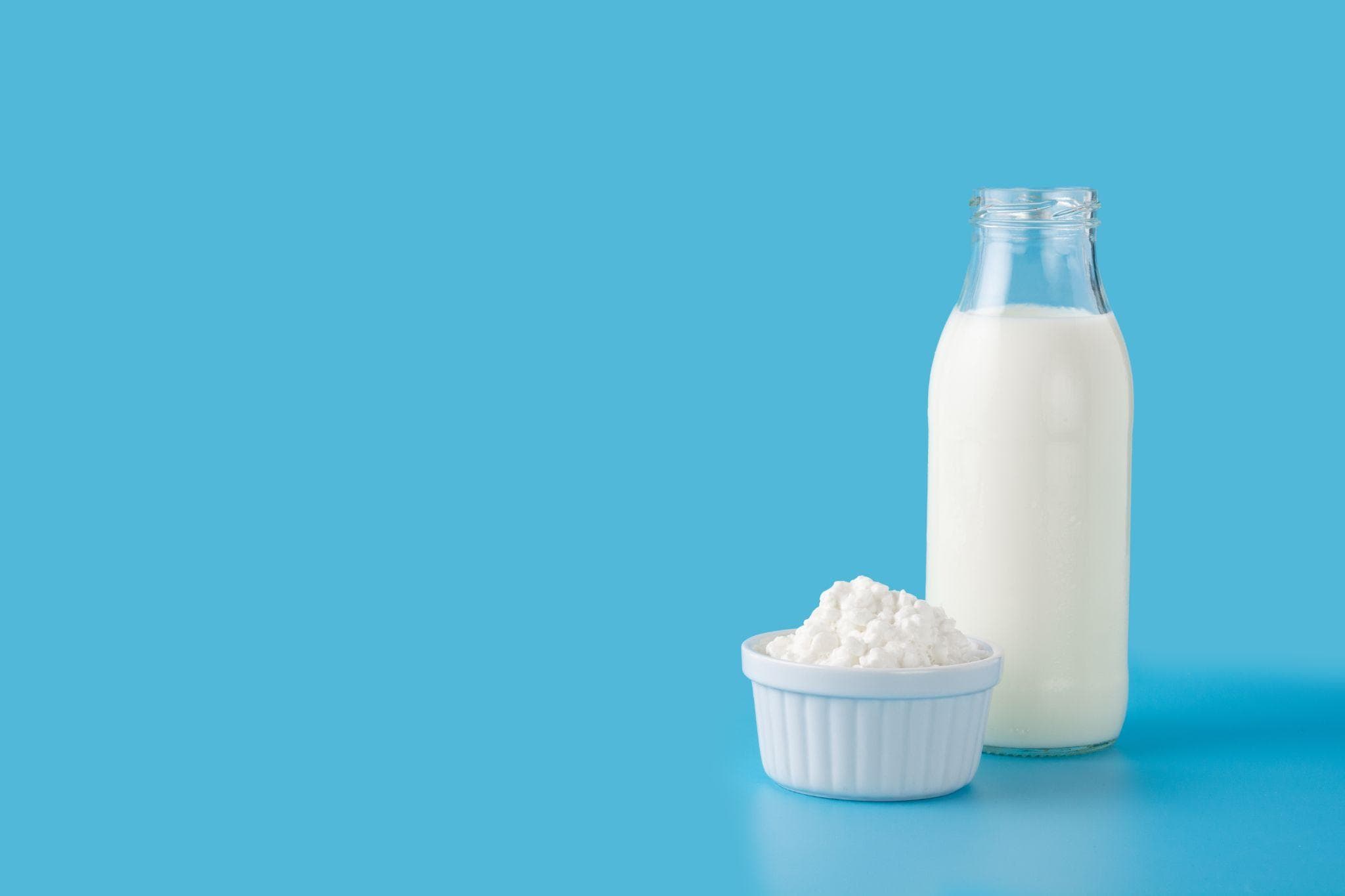 A glass bottle of milk and a bowl of cottage cheese are placed against a blue background, representing calcium-rich dairy products.