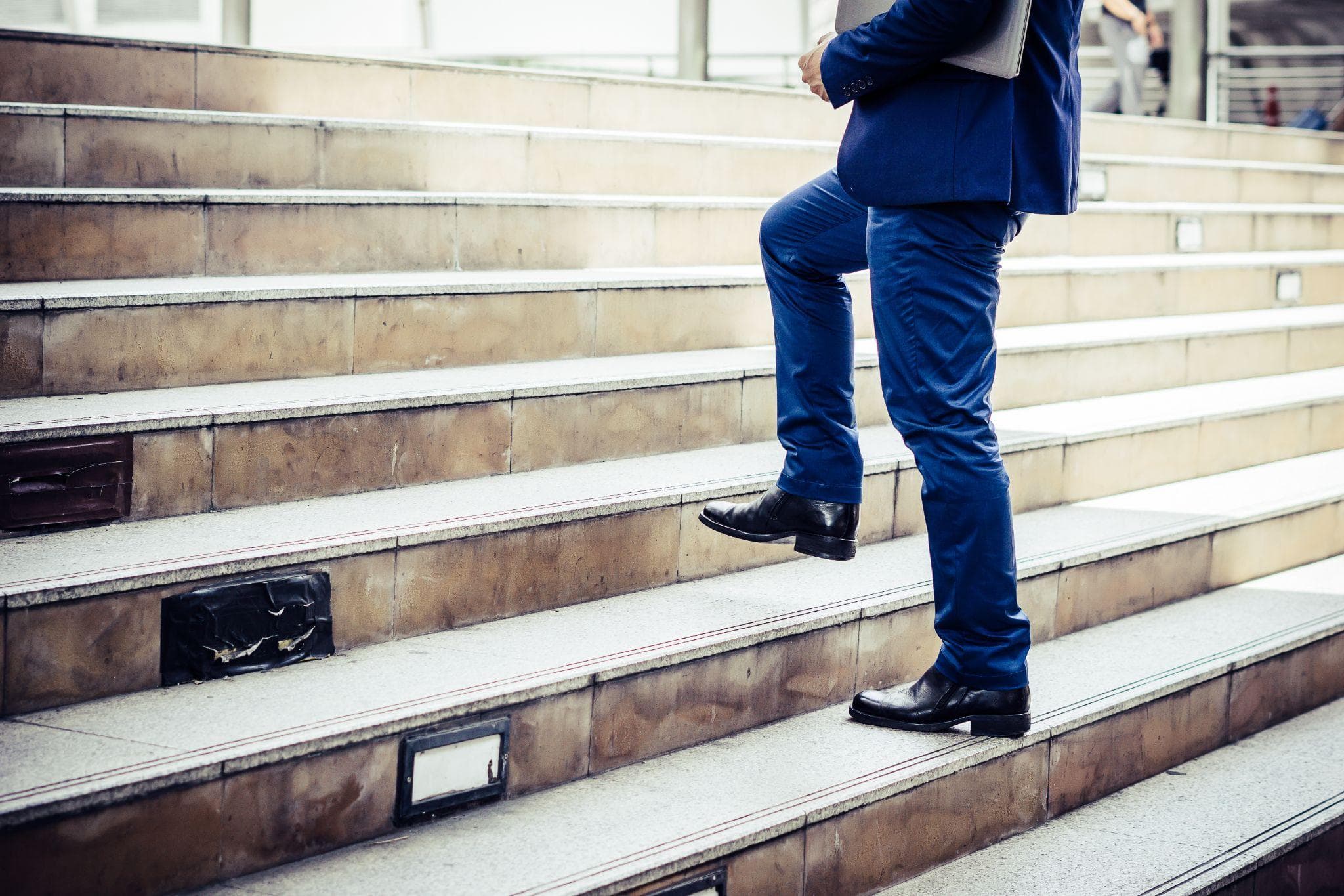 Businessman in a blue suit climbing outdoor stairs, representing improved knee mobility and functional recovery.