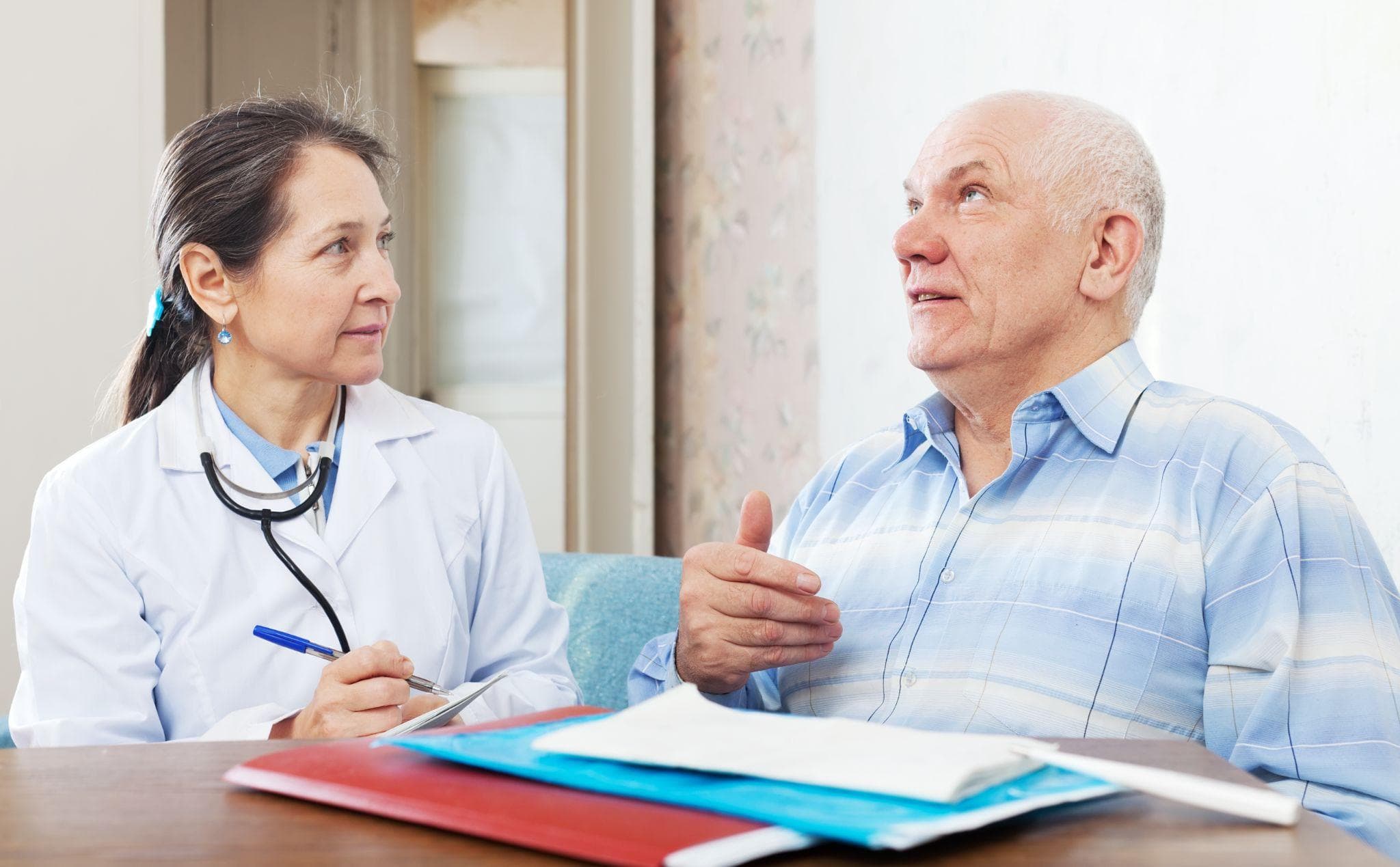 Female doctor with a stethoscope consulting an elderly male patient during a medical appointment, discussing health concerns while reviewing documents in a clinic setting.