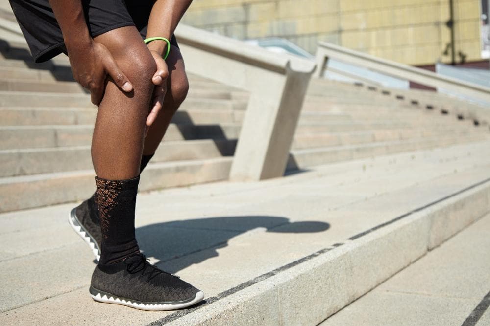 A man is bending down, holding his knee while walking, showcasing his difficulty in walking.