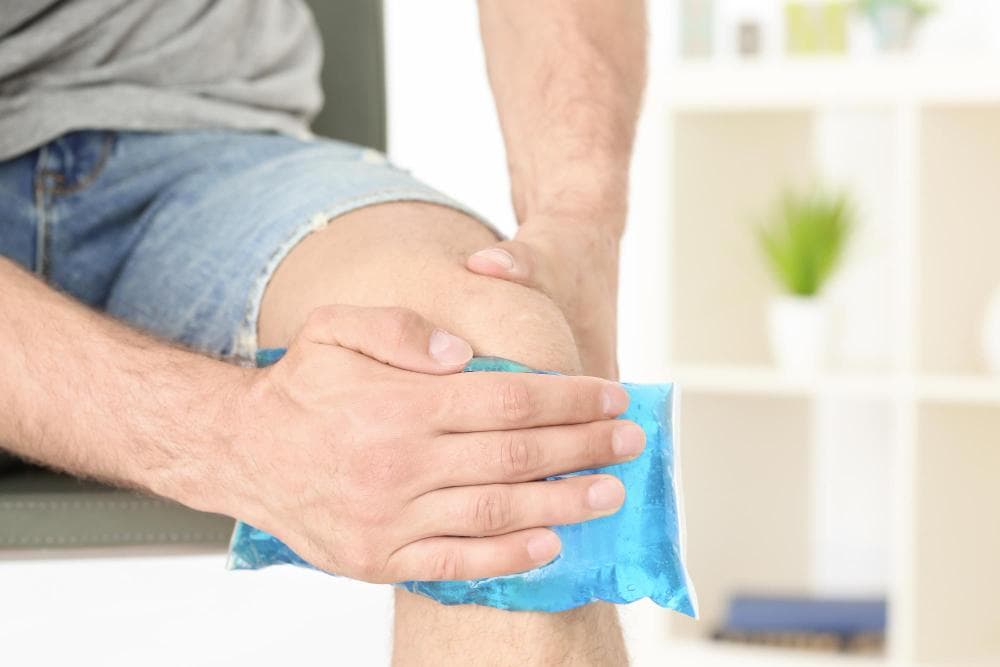 Close-up of a person applying an ice pack on the knee to reduce pain and swelling, indicating knee injury or inflammation.