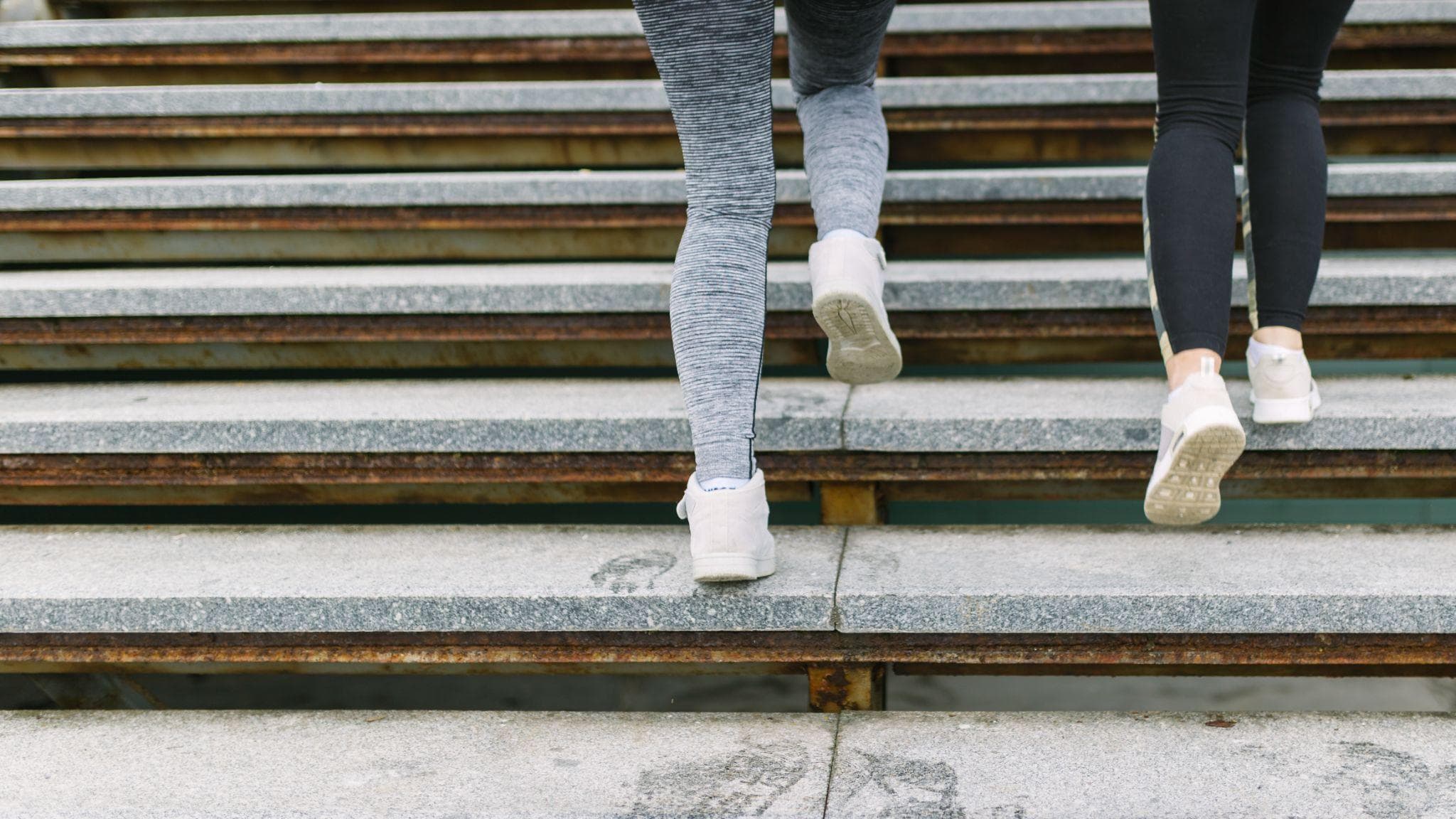 Two people wearing athletic leggings and sneakers climbing outdoor concrete stairs, focusing on leg movement and lower body activity.