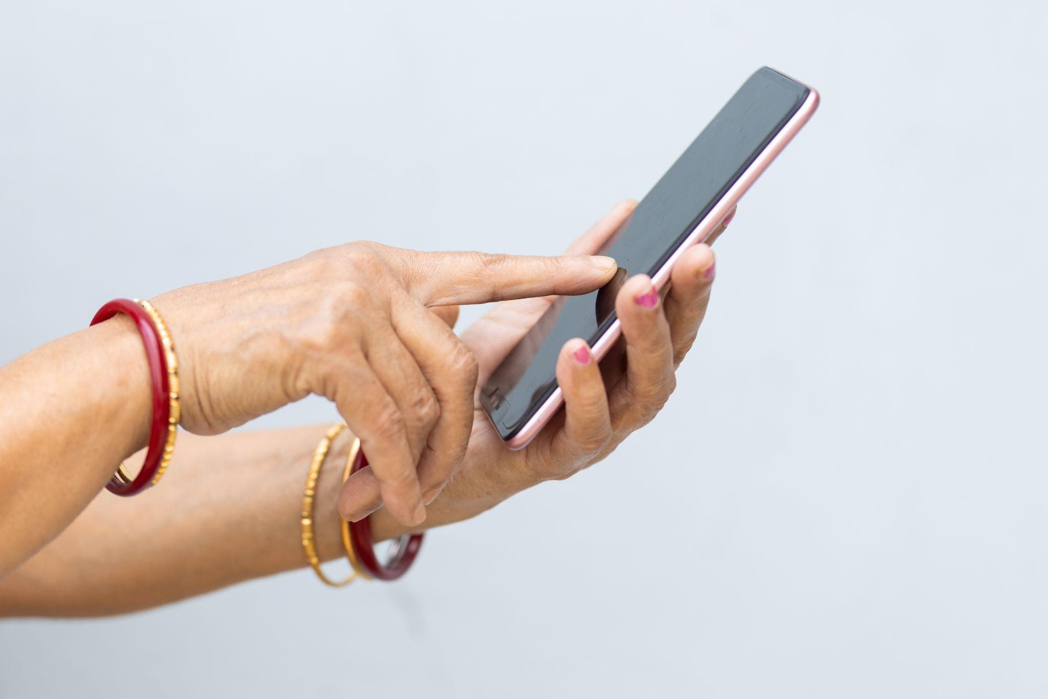 Close-up of a hand adorned with colorful bangles, tapping on a smartphone screen. The hand's positioning suggests active engagement with the device, against a neutral background.