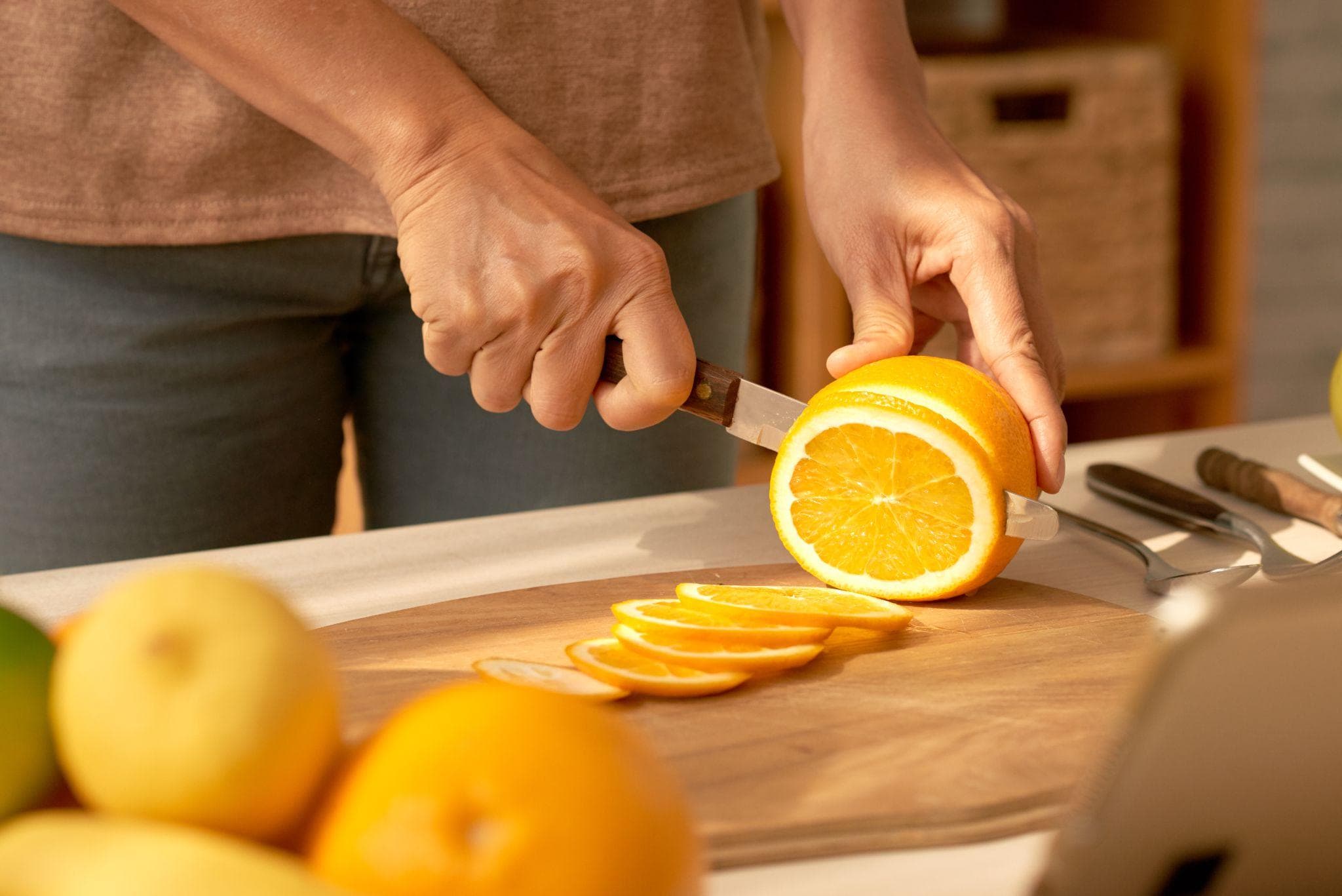 Person slicing a fresh orange on a wooden cutting board in a kitchen, highlighting vitamin C-rich fruit for a healthy diet.