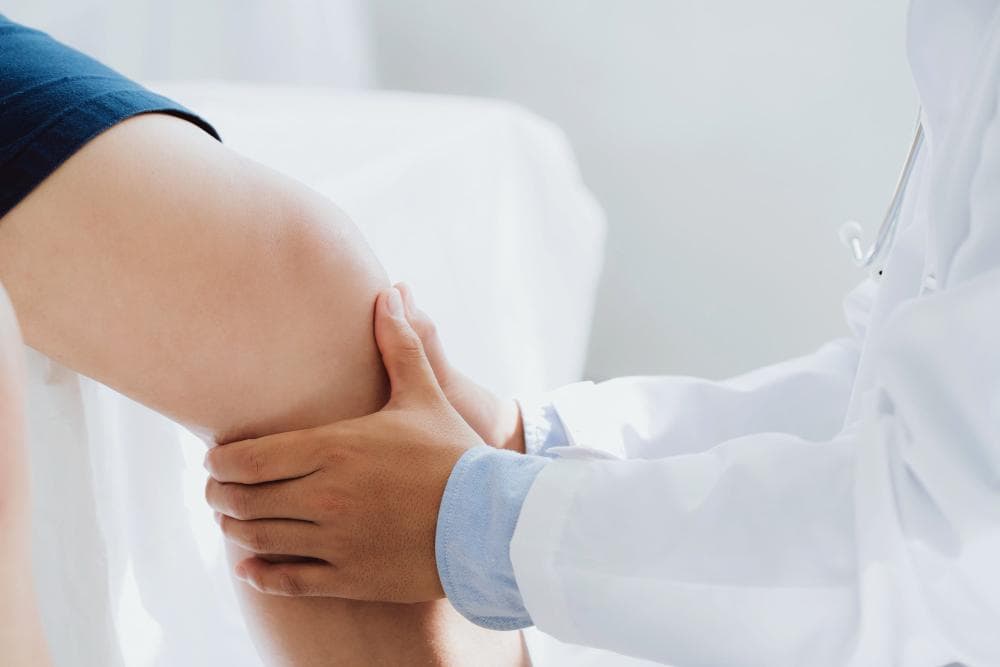 A doctor examines a patient’s knee joint by holding and assessing it for pain, swelling, or mobility issues in a clinical setting.