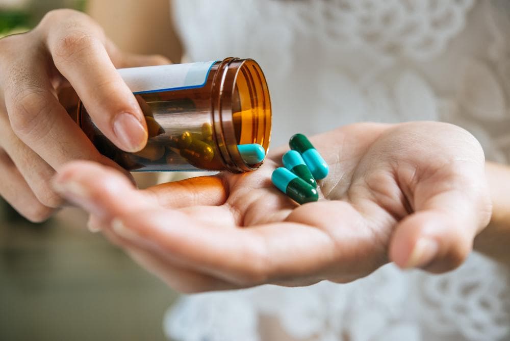 Close-up of a woman’s hands in a white dress taking out medical pills in her hands from a small bottle.