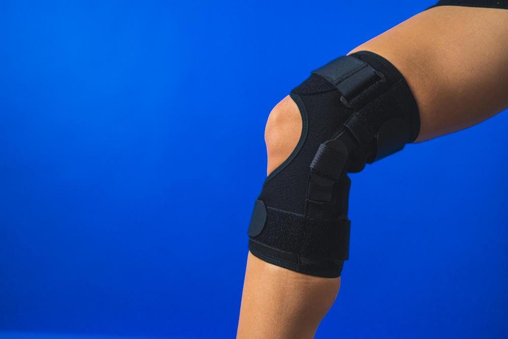 A close-up shot of the knee against the blue background, in which a man is wearing a knee brace.