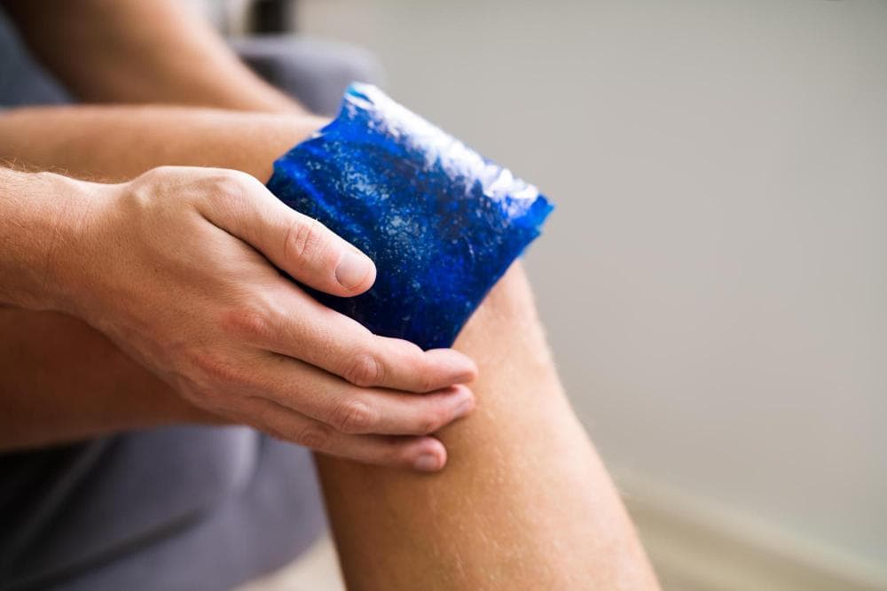 Person applying a cold gel ice pack to the knee to reduce pain and swelling, commonly used for managing knee injuries or conditions like Baker’s cyst.