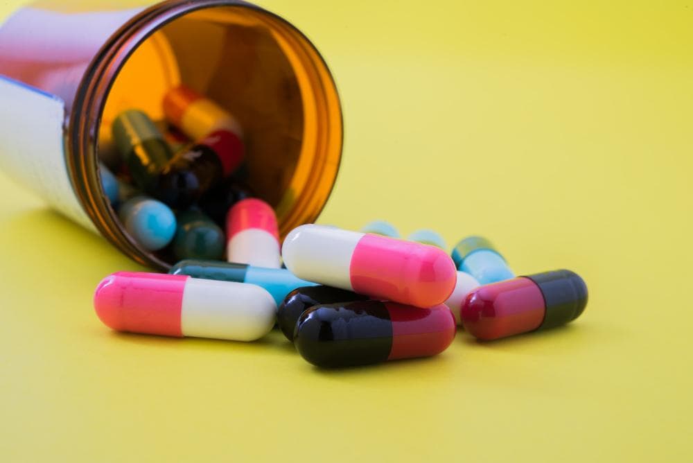A bottle of medicines is lying open, from which half of the medicines are falling out against a yellow background.