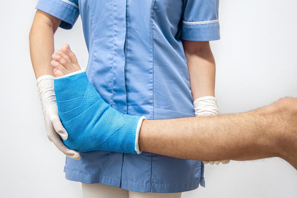 A close-up shot of a female doctor examining the fractured foot of a male patient with a blue casket on it.