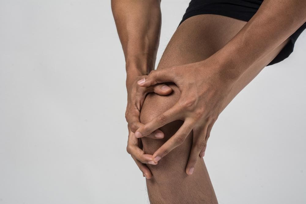 A close-up shot of a man’s leg against a white background. He is holding his knee with both his hands.