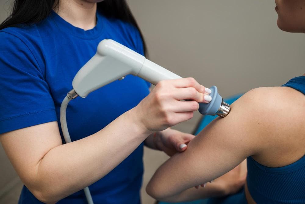Physiotherapist performing shockwave therapy on a patient’s shoulder using a handheld device to treat calcific tendinitis and relieve pain and inflammation.