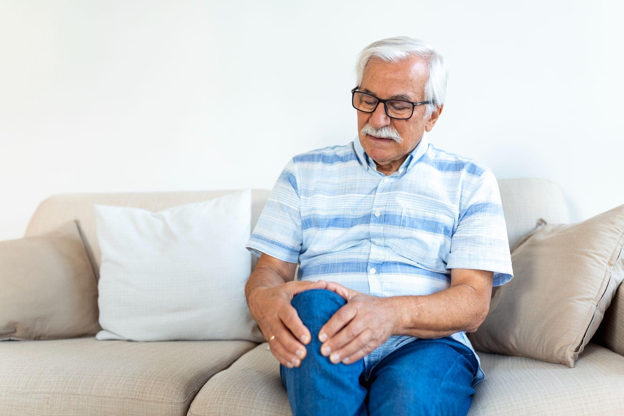 An elderly man sitting at home holding his knee in pain.